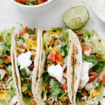 Mexican-spiced ground beef tacos with shredded lettuce, homemade pico de gallo, cheddar cheese, and sour cream stuffed into grilled flour tortillas.